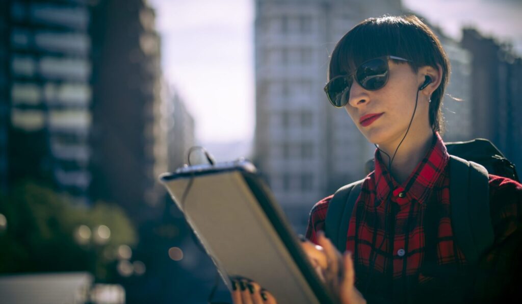 Mujer joven con mochila usa tableta al aire libre.