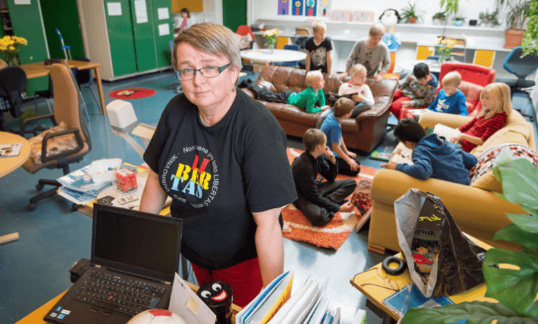 Maestra en aula con niños sentados en sofás. Ambiente relajado y laptop en primer plano. Borrador automático.
